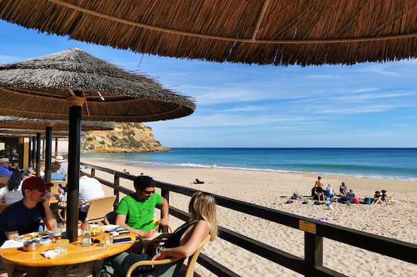 A beachside restaurant with thatched umbrellas and wooden tables overlooking the ocean.