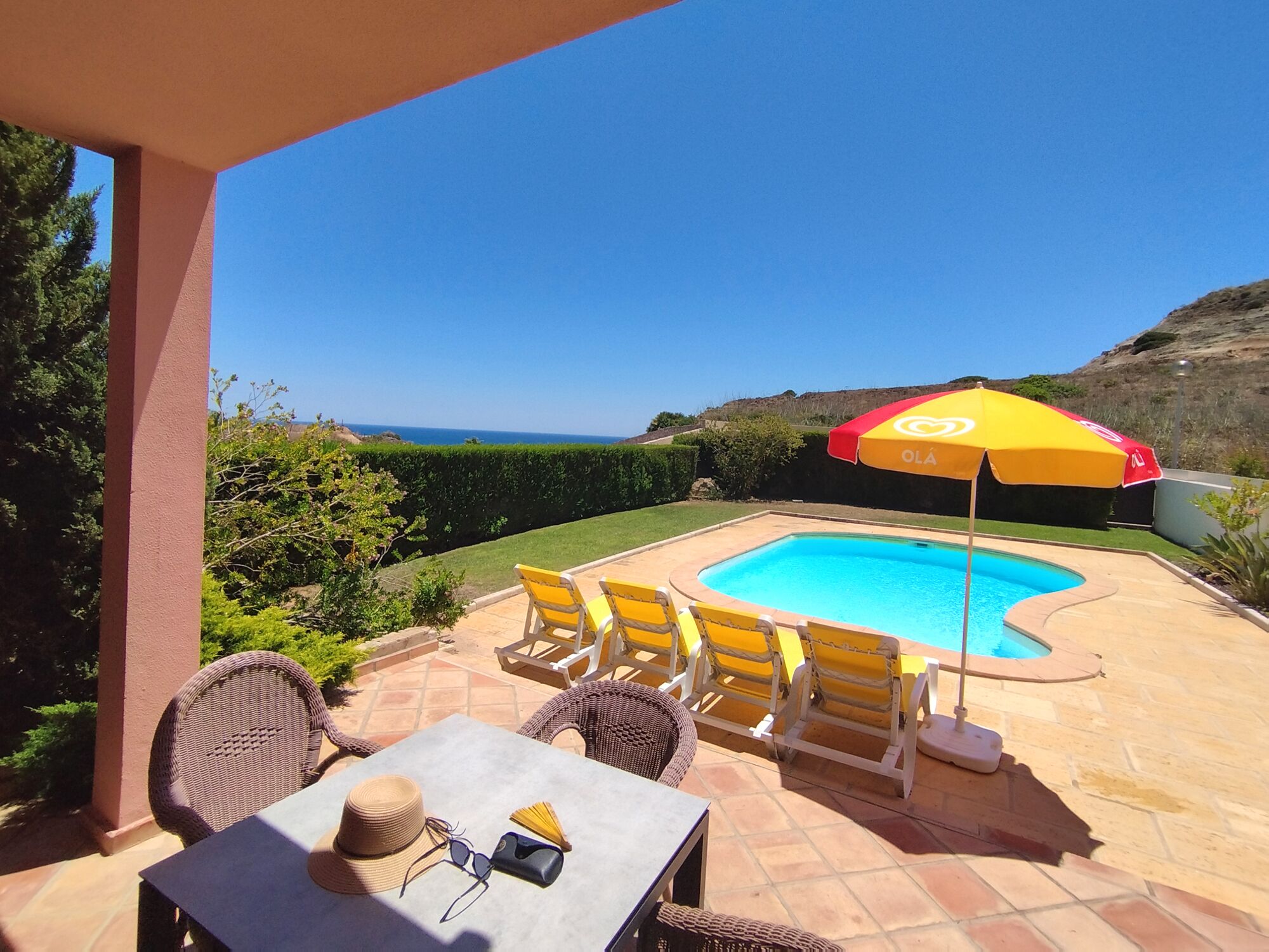 A poolside area with a table, chairs, and an umbrella.
