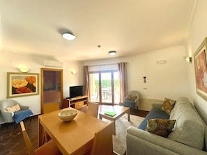 A living room with a sofa, a dining table, a TV, and a sliding glass door leading to an outdoor area.