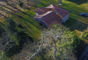 Vista aérea de uma casa com telhado inclinado, cercada por um gramado bem cuidado e árvores.