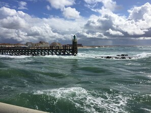 Um cais que se estende para o mar, com um farol no final, rodeado por edifícios e um céu nublado.