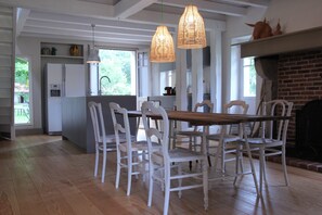 A dining area with a wooden table and white chairs, a kitchen in the background, and a brick fireplace. - Large **** family house in the middle of a huge centennial park near ocean and golf course (Messanges)