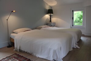 Quarto com duas camas, uma mesa de cabeceira, um abajur e janela com vista para o verde.