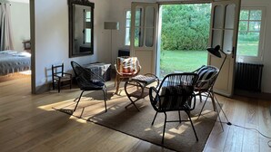 Une pièce dotée d’un plancher en bois, d’un grand miroir, d’une table avec des chaises et offrant une vue sur un jardin grâce à des portes ouvertes.
