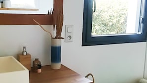 Un baño con tocador de madera, un espejo, una ventana con vista a vegetación y una toalla verde sobre una repisa.