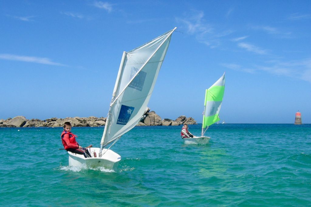Two sailboats on calm waters with rocky coastline in the background.