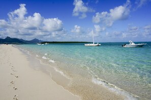 Una playa con agua turquesa cristalina, una orilla arenosa y barcos anclados en la distancia.