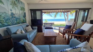 A living room with a sofa, armchairs, and a coffee table. There is a view of the beach through an open door. - Pointe D Esny: House / Villa - Pointe d''Esny (Pointe d'Esny)