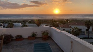 A rooftop terrace with a view of the sunset over the ocean, potted plants, and a pool. - SEAFRONT APARTMENT (Tarifa)