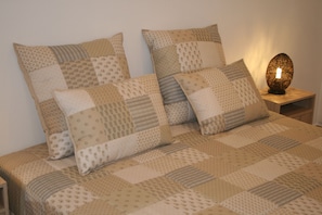 A bed with a patchwork quilt and several pillows, a bedside table with a lamp, and a wooden nightstand.