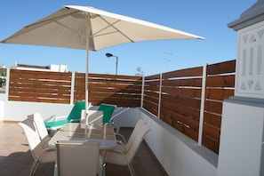 An outdoor patio with a table and chairs, a large umbrella, and a wooden fence.