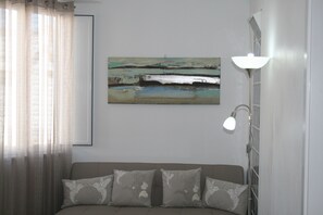 A bedroom with a bed, a painting on the wall, and a floor lamp.