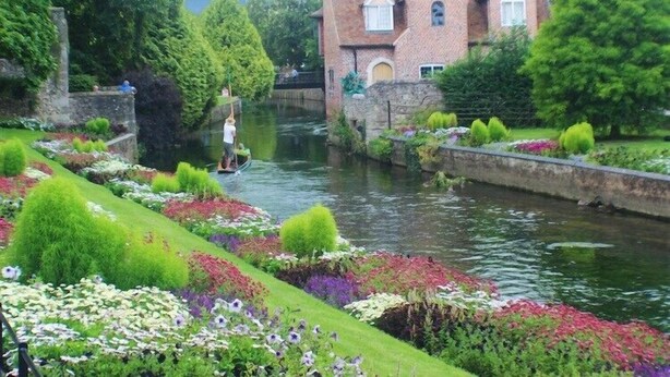Un canal bordé de parterres de fleurs, avec un bâtiment en briques en arrière-plan.
