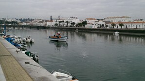A calm waterfront with boats docked along the quay, a row of buildings in the background, and a clear sky. - Villa Magaída, AC, private space with pool (Luz (Luz de Tavira))