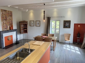 Une cuisine moderne dotée d’un évier encastré, d’une table à manger en bois, de chaises en osier et d’un mur d’accent rouge.