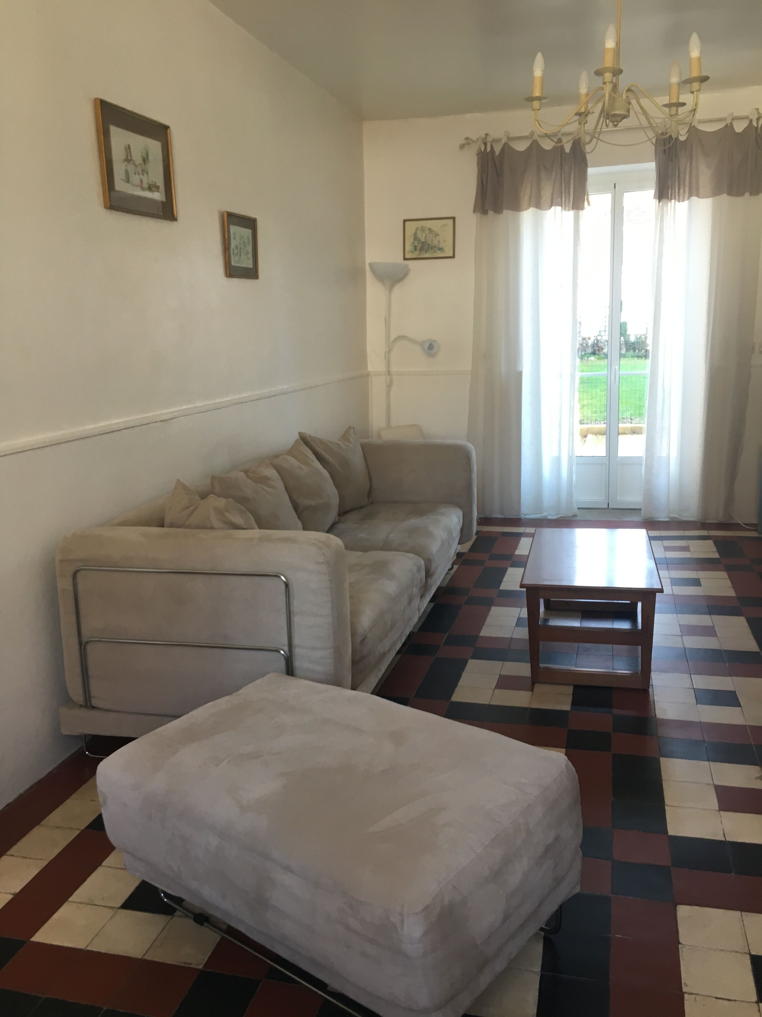 Sala de estar com sofá, mesa de centro, piso estampado e vista pela janela com cortinas.