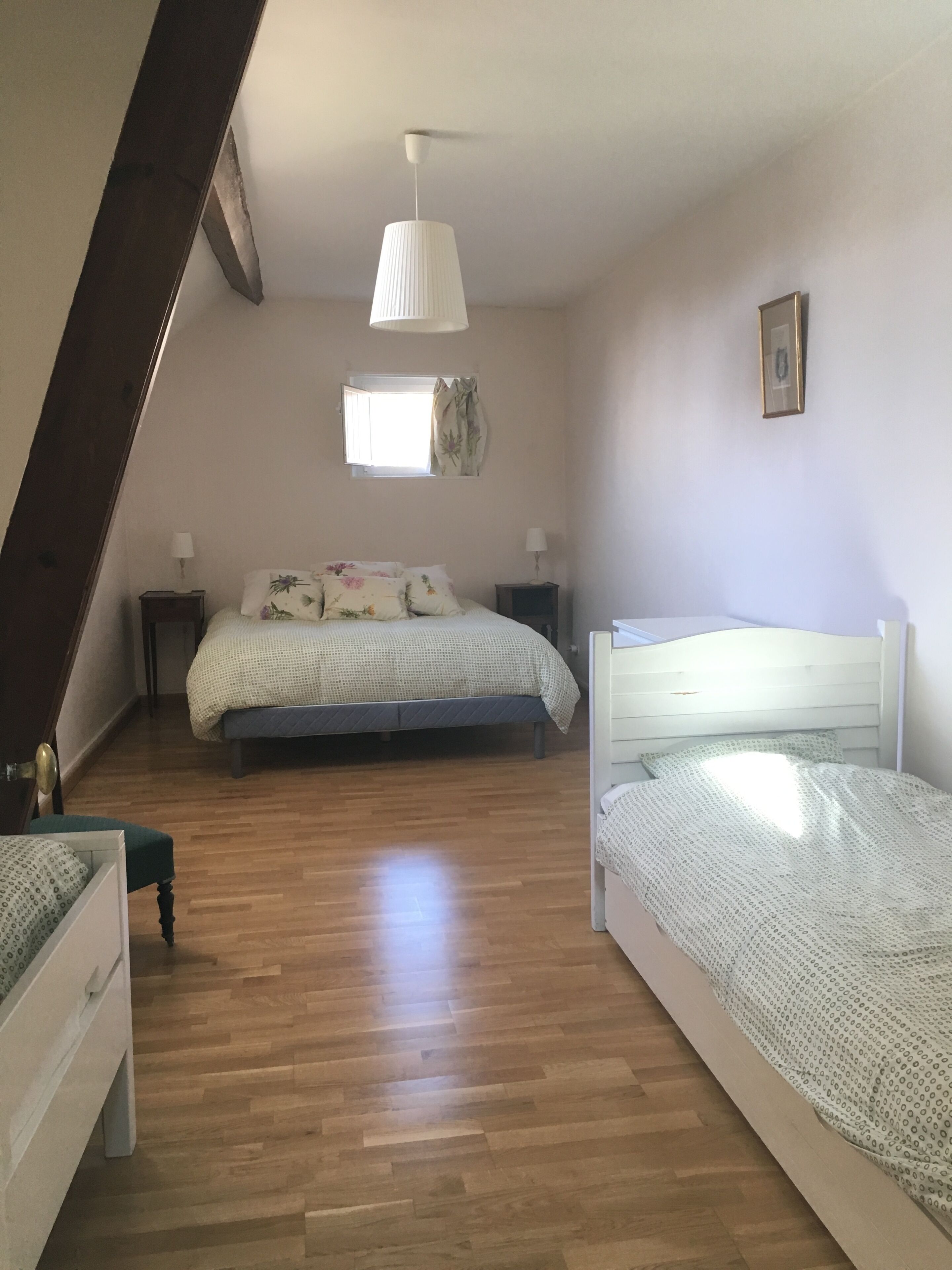 A bedroom with a sloped ceiling, a bed with floral bedding, a bedside table with a lamp, and a window with curtains.