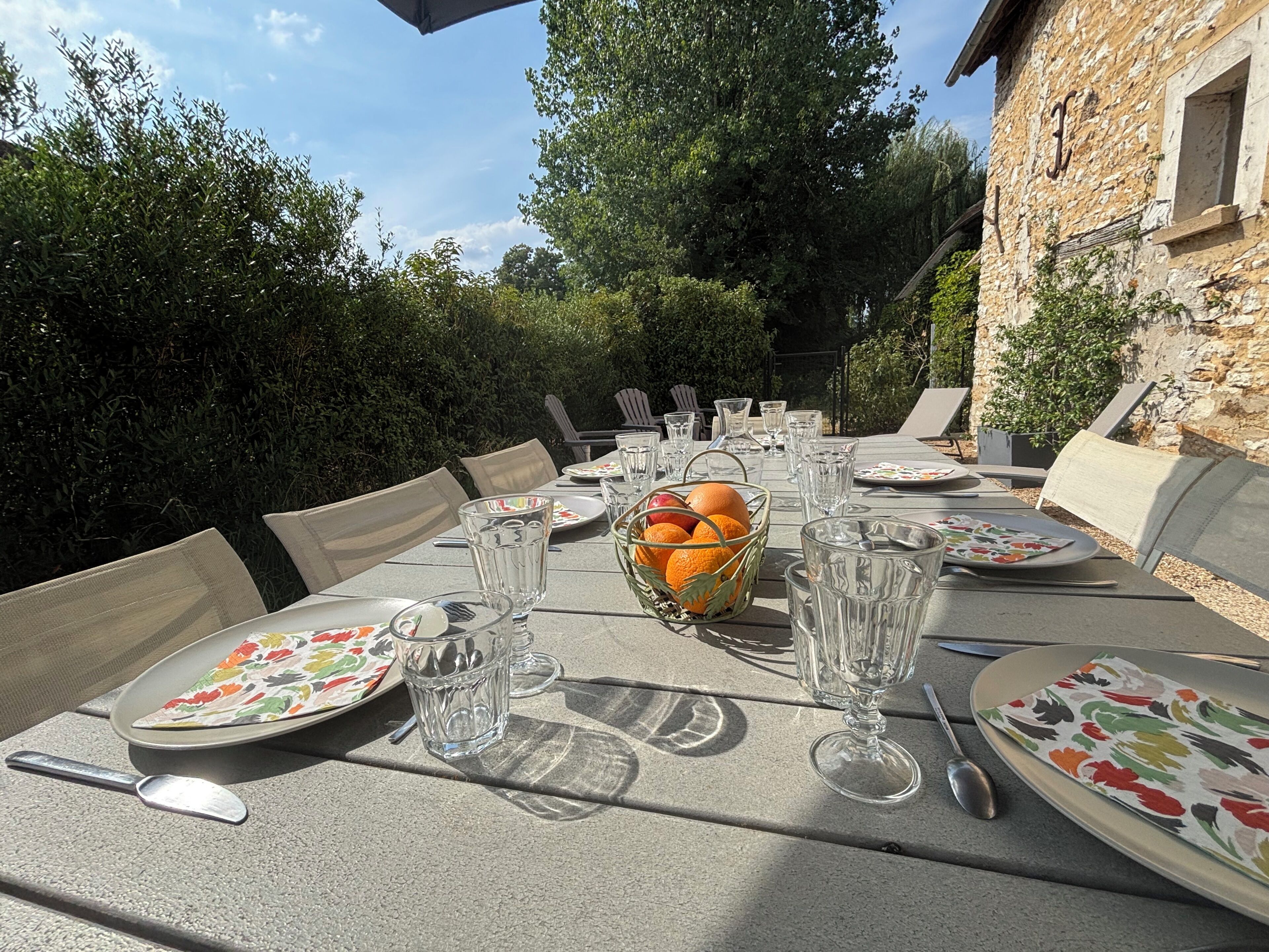 Un espace de restauration en plein air, avec des tables dressées pour le repas, entouré de verdure et de murs en pierre.