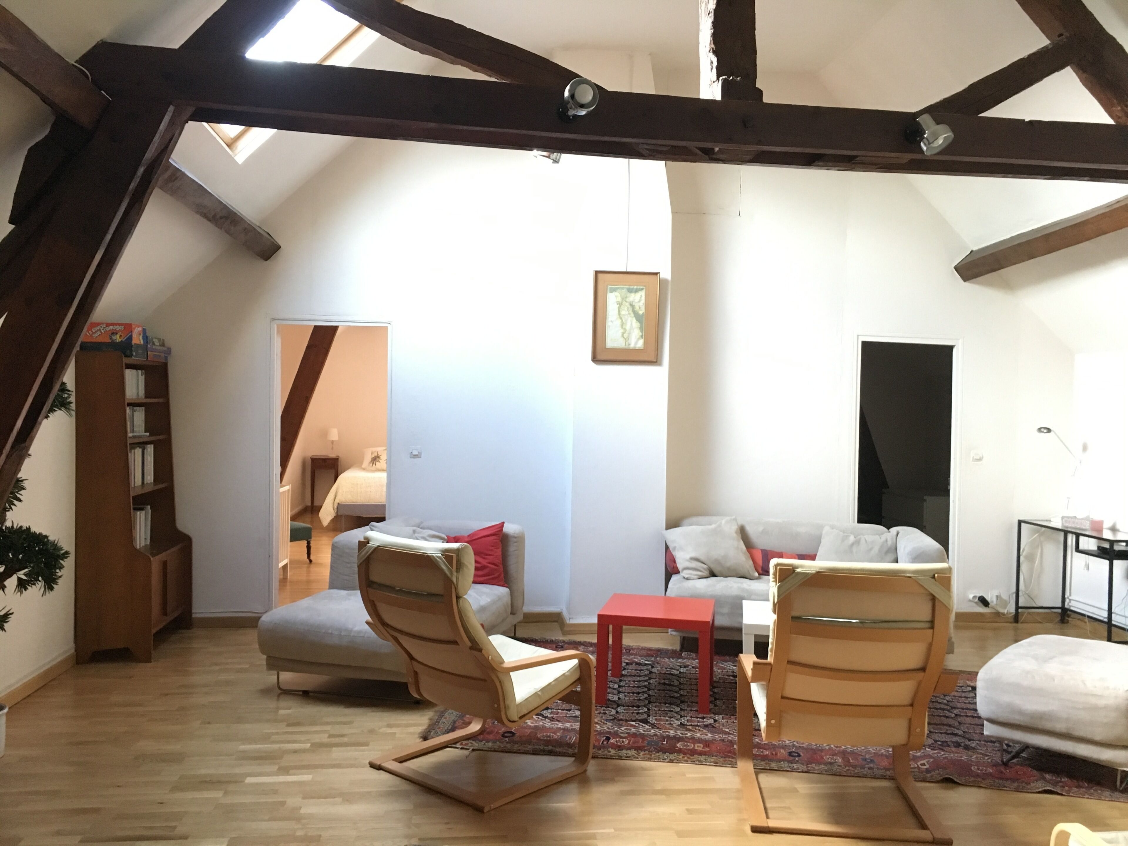 Un espacio tipo loft con vigas de madera a la vista, techo alto, un sofá, dos sillones mecedores, una mesita y una estantería.