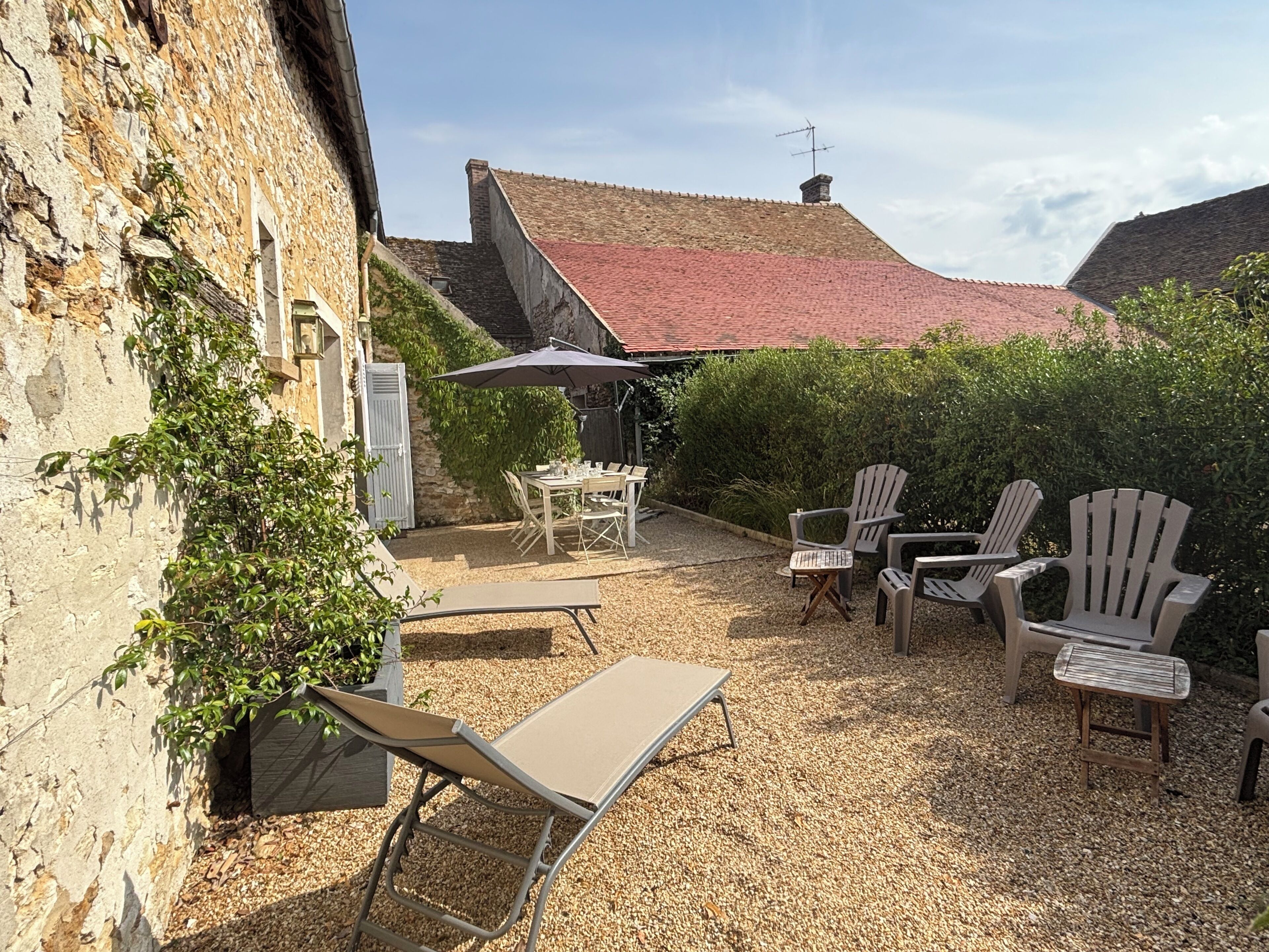 Une cour intérieure aménagée avec du mobilier d’extérieur, une table et des chaises, le tout entouré de murs en pierre et de verdure.