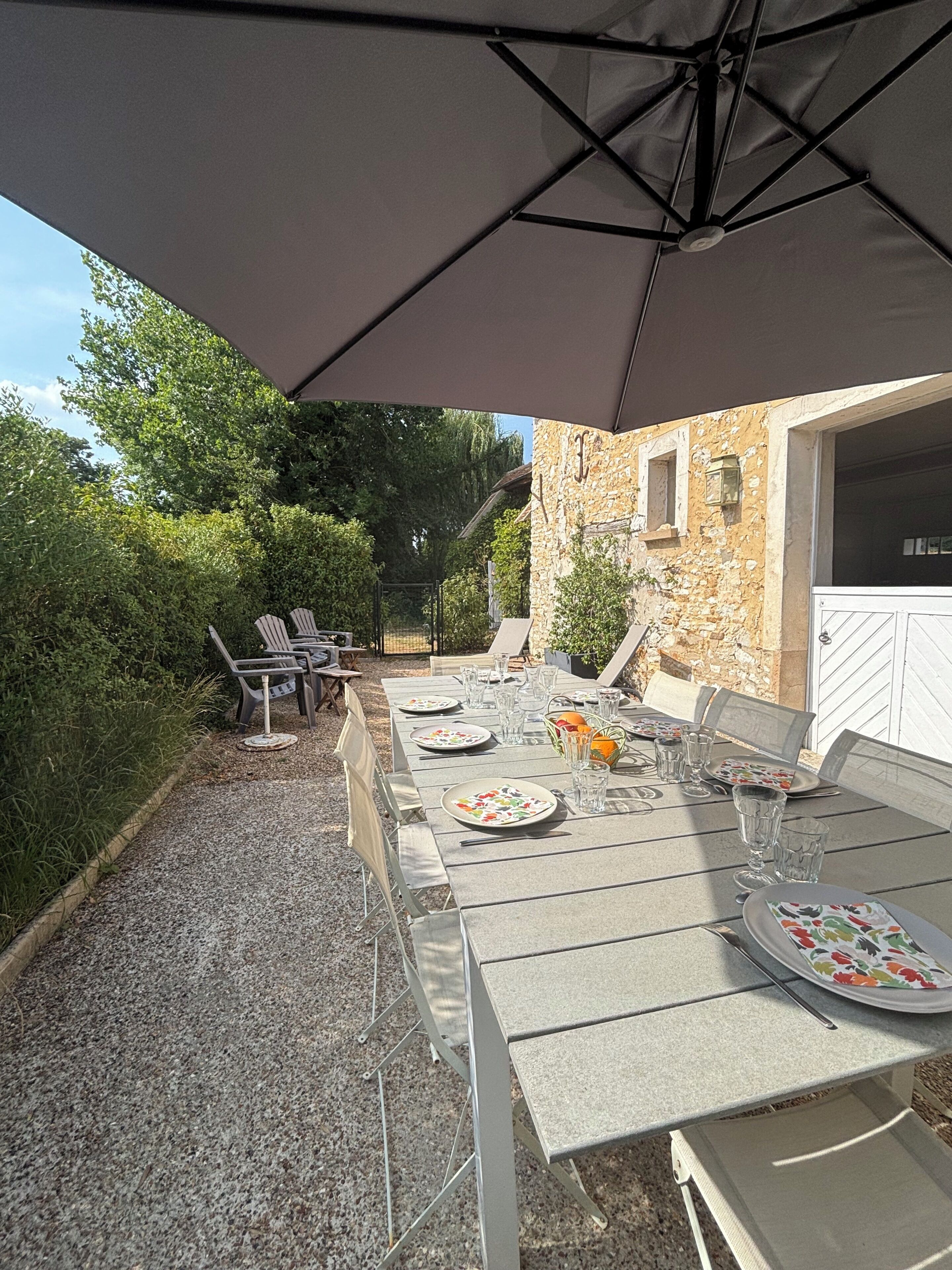 An outdoor dining area with a table set for four, surrounded by chairs, under a large umbrella.