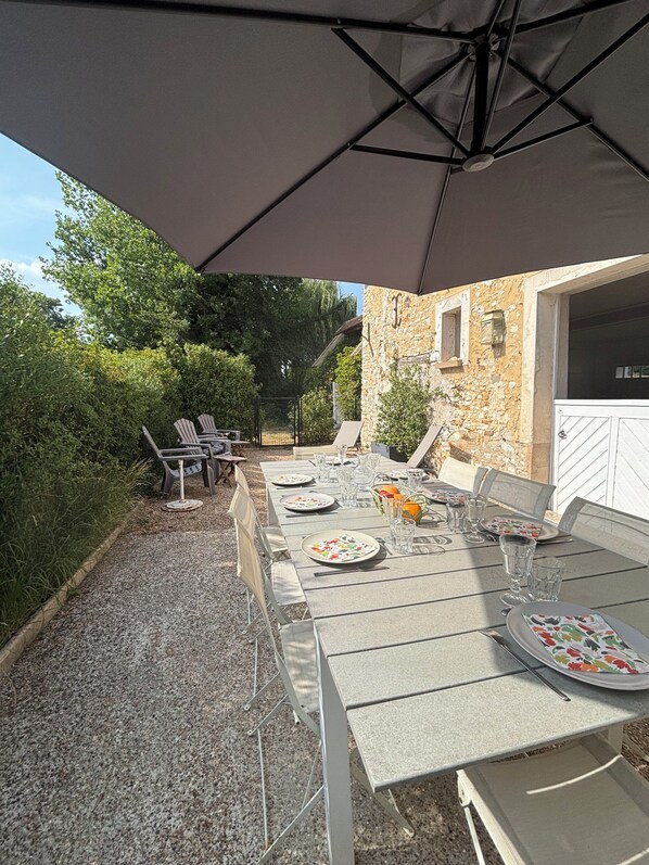 An outdoor dining area with a table set for four, surrounded by chairs, under a large umbrella.
