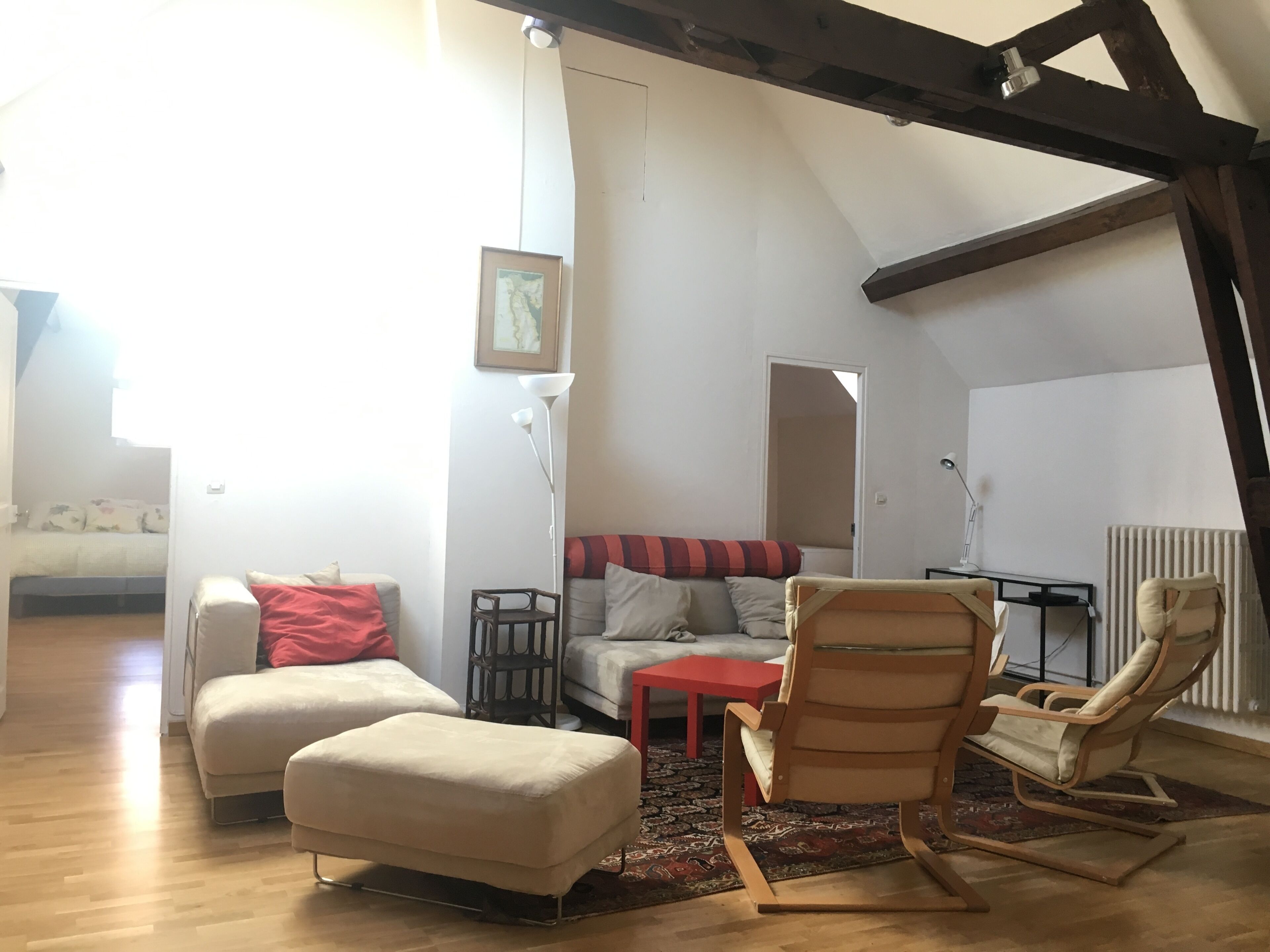 Ein Loft mit hohen Decken, freiliegenden Balken, einer Couch, Hocker, einem Schaukelstuhl und einem kleinen Tisch.