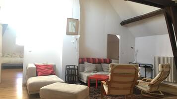 Un living in stile loft con soffitto alto, travi a vista, divano, poggiapiedi, poltrona a dondolo e un tavolino.