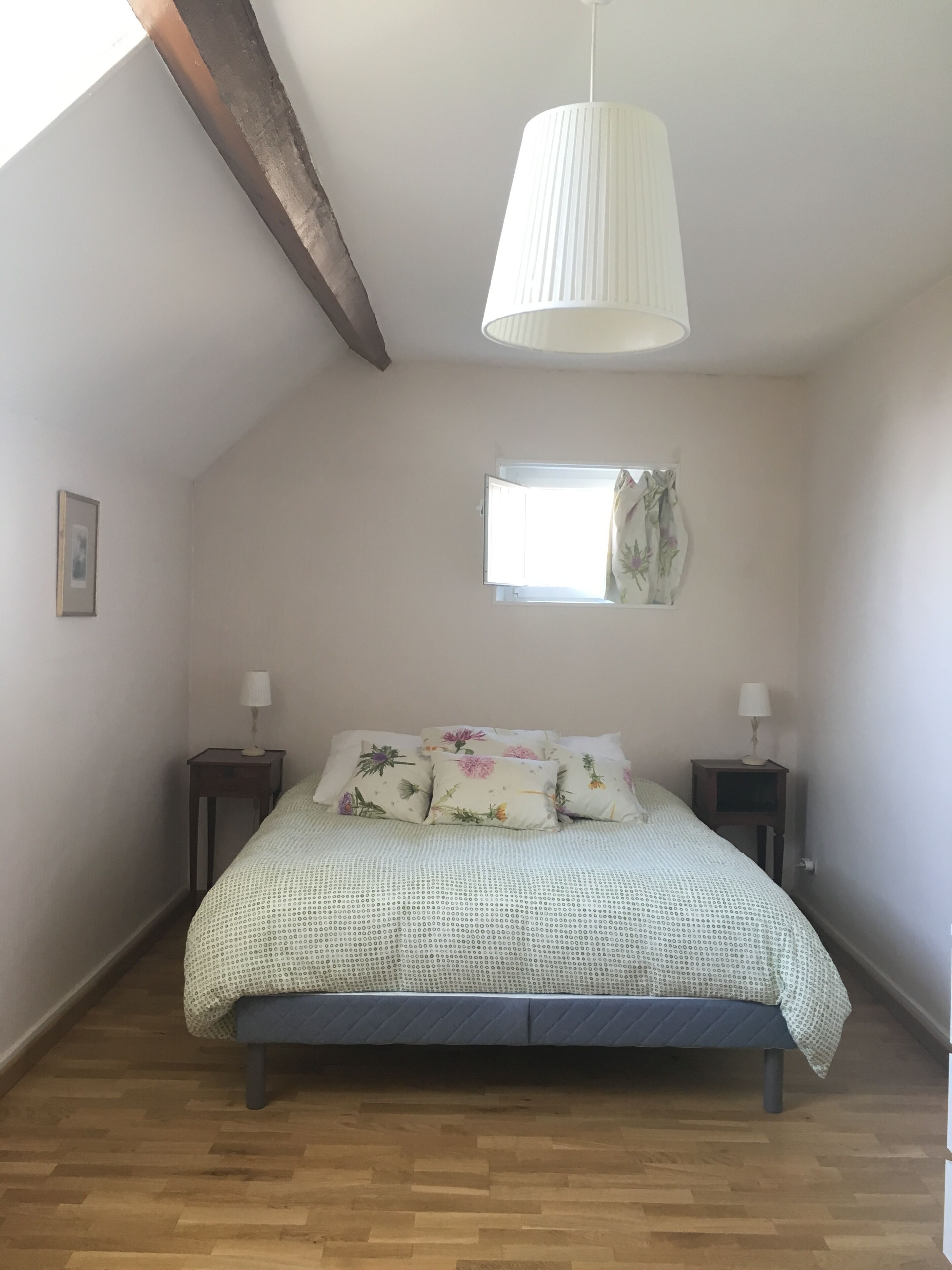 Ein Schlafzimmer mit einem Bett, zwei Nachttischen, einer Pendelleuchte, einem Fenster und einem Holzboden.