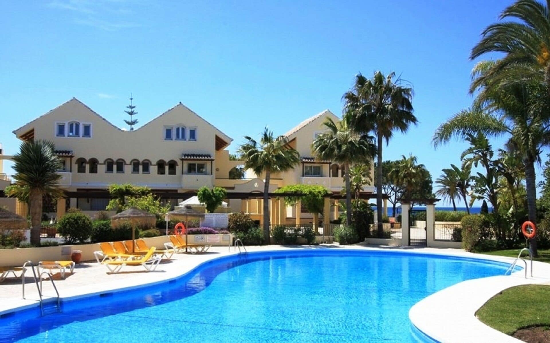A hotel with a swimming pool, palm trees, and a clear blue sky.