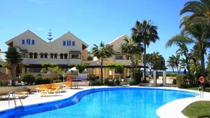 Un hôtel doté d’une piscine, de palmiers et surplombant un ciel bleu azur.