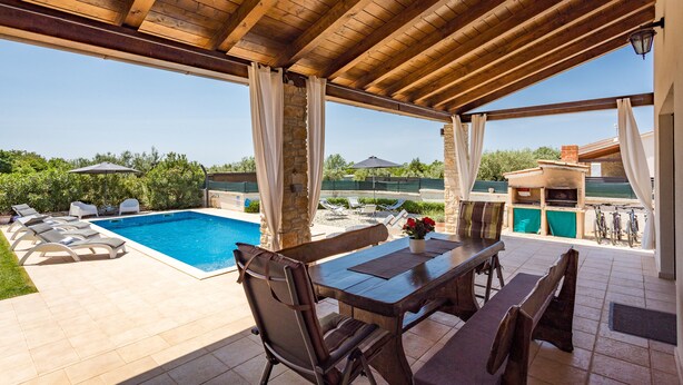 Un patio couvert avec une piscine, un espace salon extérieur et un coin barbecue.