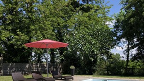 A rectangular swimming pool with a wooden deck, two lounge chairs, and a red umbrella. - A charming stone house with unique views of the Dordogne River (Bergerac)