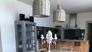 A dining area with a wooden table and chairs, a chandelier, and a kitchen in the background. - A charming stone house with unique views of the Dordogne River (Bergerac)