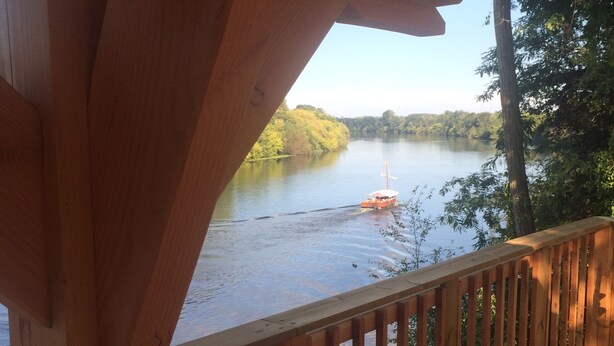 A wooden deck overlooking a calm river with a boat. - A charming stone house with unique views of the Dordogne River (Bergerac)