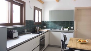 A compact kitchen with a toaster, sink, and wooden dining table with a fruit bowl. - Large and quiet detached house in the historic center - CIN IT091095C2000S3477 (Tortolì)