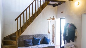 A staircase leading to a loft bedroom with a wooden staircase, a sofa with blue cushions, and a small table with a basket. - Large and quiet detached house in the historic center - CIN IT091095C2000S3477 (Tortolì)