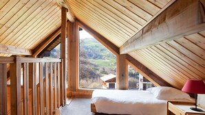 A cozy attic bedroom with wooden beams, two beds, a nightstand, and a large window offering a view of the countryside. - Lovely flat (sleeps 6/8) in chalet 300 m from slopes with shared sauna  (Les Avanchers-Valmorel)