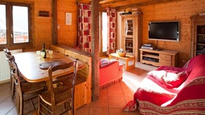 A wooden cabin interior with a dining table, chairs, a sofa, a television, and a fireplace. - Lovely flat (sleeps 6/8) in chalet 300 m from slopes with shared sauna  (Les Avanchers-Valmorel)