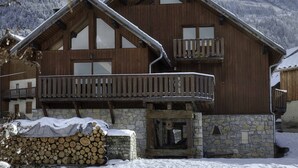 A wooden chalet with a balcony, stone foundation, and a view of snow-covered mountains. - Lovely flat (sleeps 6/8) in chalet 300 m from slopes with shared sauna  (Les Avanchers-Valmorel)