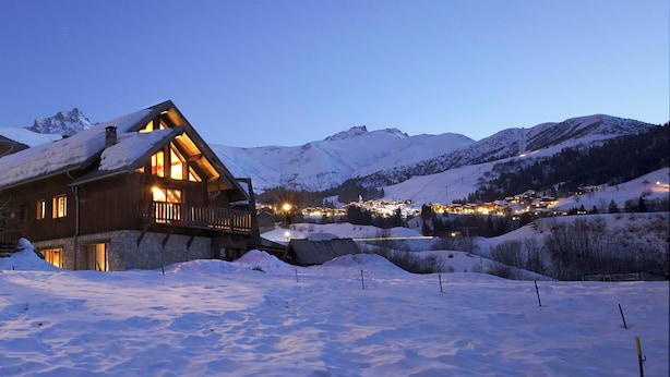 A wooden lodge with a stone foundation, surrounded by snow-covered mountains and lit by warm interior lights. - Lovely flat (sleeps 6/8) in chalet 300 m from slopes with shared sauna  (Les Avanchers-Valmorel)
