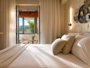 A bedroom with a bed, curtains, a window, a table with a vase, and a wall-mounted light fixture.
