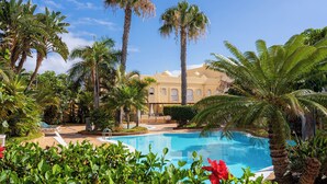 A pool surrounded by palm trees and a building with a yellow facade. - Apartment with WIFI  in a beatiful complex (Corralejo)