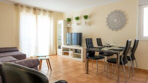 A living room with a sofa, a glass coffee table, a TV, and a dining area with chairs and a table. - Apartment with WIFI  in a beatiful complex (Corralejo)