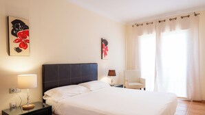 A hotel room with a bed, a nightstand with a lamp, a chair, and two wall art pieces. - Apartment with WIFI  in a beatiful complex (Corralejo)