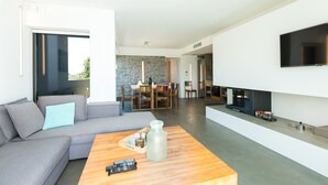 Een moderne woonkamer met een grijze bank, een houten salontafel, een flatscreen-televisie aan de muur en een stenen achtergrond.
