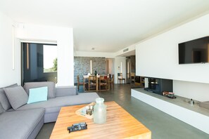 Een moderne woonkamer met een grijze bank, een houten salontafel, een flatscreen-televisie aan de muur en een stenen achtergrond.