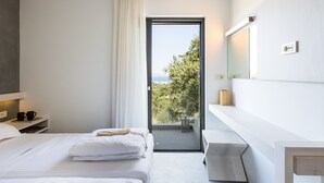 Een moderne hotelkamer met een bed, een badkamer met een spiegel en een balkon met uitzicht op groen.