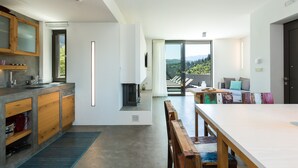 Een moderne keuken met een groot kookeiland, een eethoek met een houten tafel, en uitzicht op een balkon met zitplaatsen.