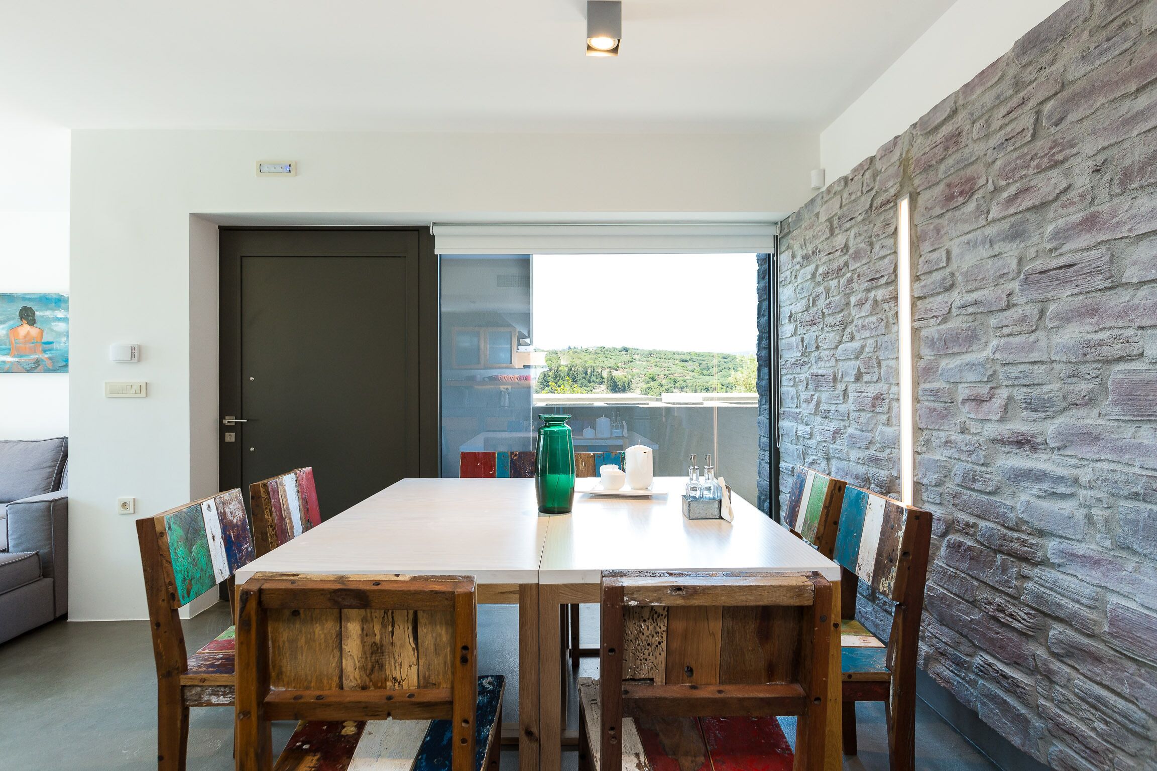 Un coin repas avec une table blanche, des chaises en bois et un mur en pierre.